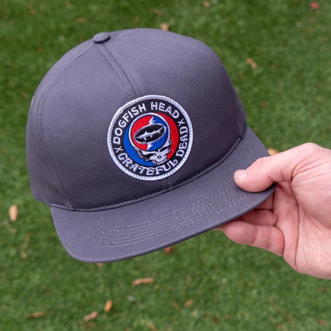 A charcoal colored flat brim hat with the Dogfish Head and Grateful Dead collaboration logo on the front.