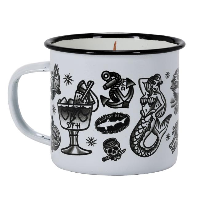 A white enamel mug candle featuring vintage-style black-and-white tattoo graphics, including anchors, mermaids, citrus, and Dogfish Head branding, with a wooden wick in the center.
