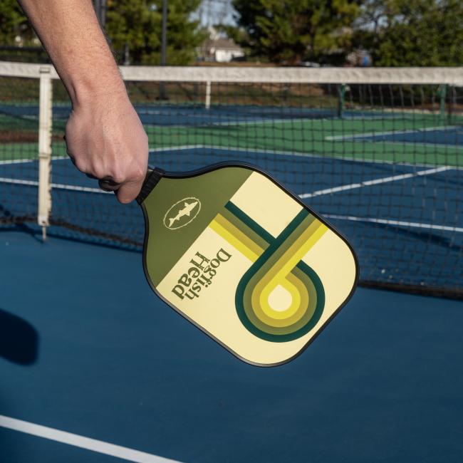 Dogfish Head Pickle Ball Paddle in a Green and White Retro Design In The Hand of a Pickle Ball Player