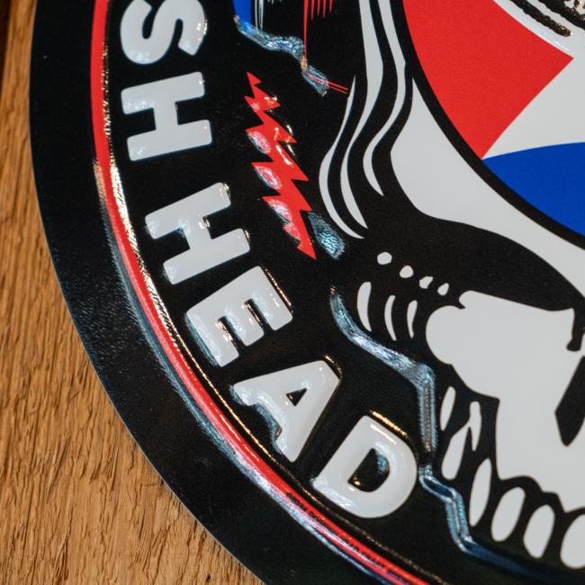 Circular metal wall tacker with the Dogfish Head x Grateful Dead skull with headphones and shark & shield logo 