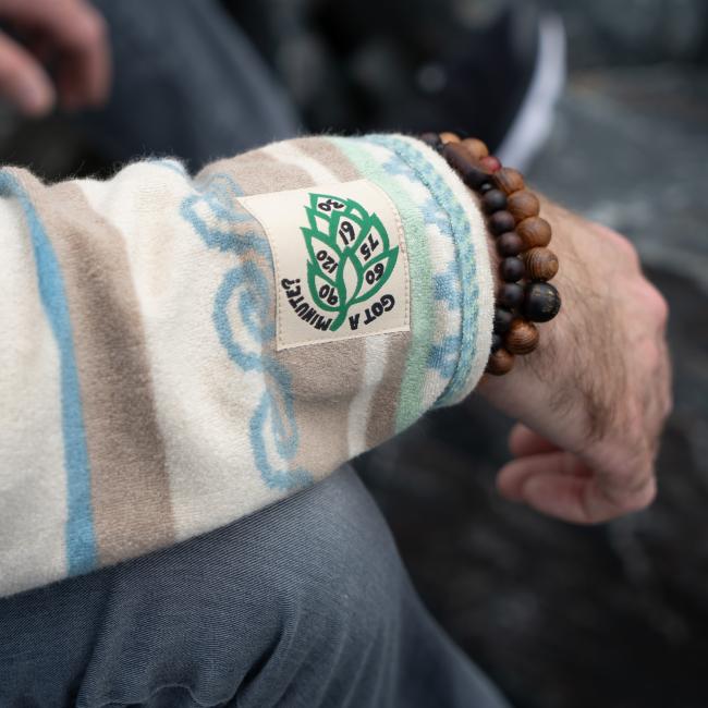 Male model wearing Howler multi stripe terry cloth stripe hoodie. Close up of embroidered Got a Minute hop on sleeve 