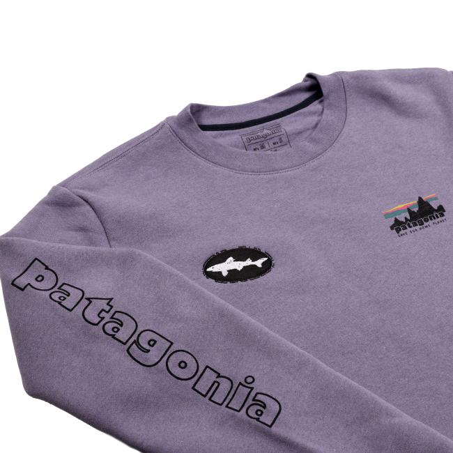 Angled close-up of the purple sweatshirt showing the chest details with the Dogfish Head shark patch and Patagonia graphic, along with the bold black “patagonia” text printed down the sleeve.