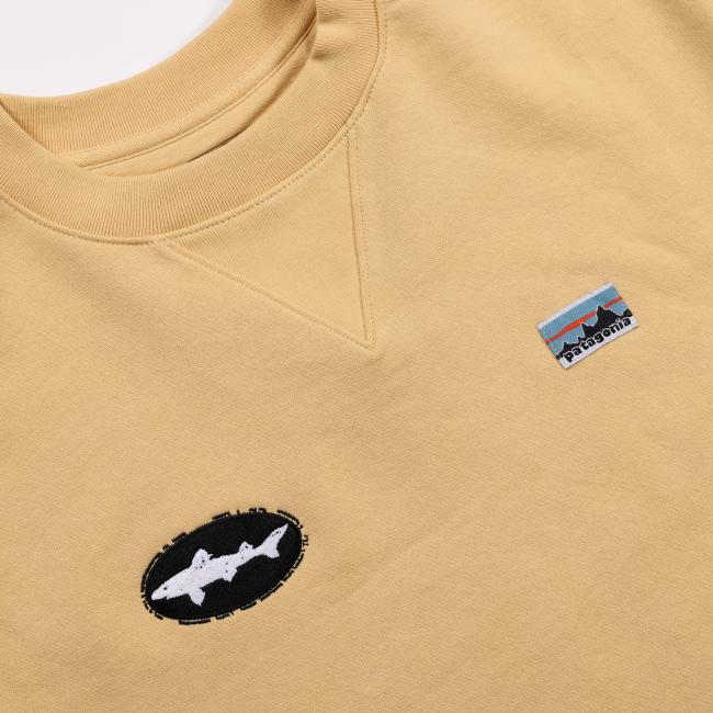 Close-up of the yellow sweatshirt’s chest area showing the black Dogfish Head shark patch and the rectangular Patagonia mountain logo patch stitched side by side.