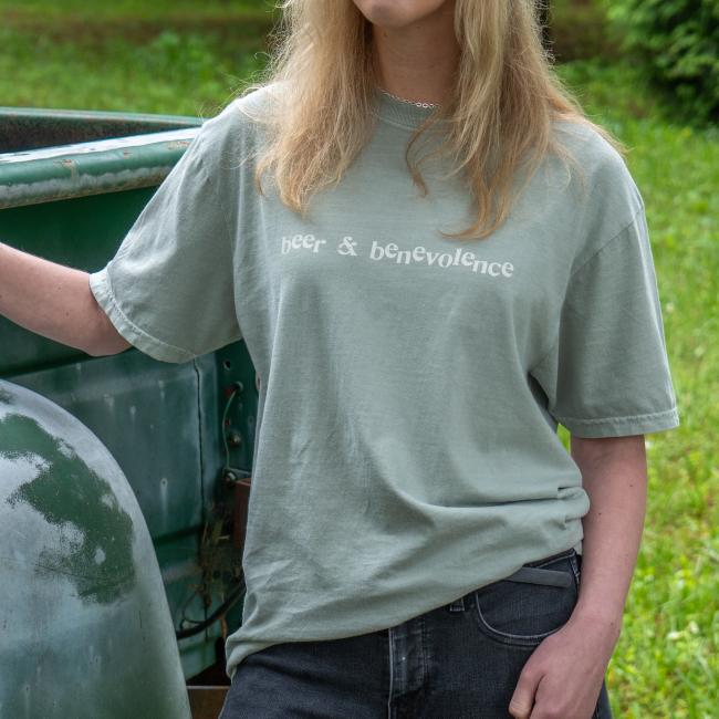 A person wears a light sage green t-shirt with the text