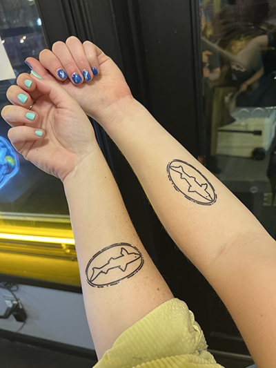 Two arms with Dogfish Shark and Shield tattooed on their forearms